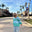 Child in a striped sweater standing on a sidewalk with palm trees and a building in the background