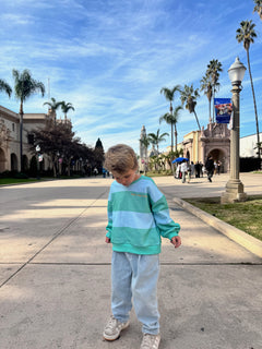 Child in a striped sweater standing on a sidewalk with palm trees and a building in the background